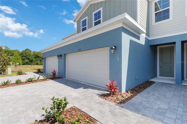 view of side of home with a garage, board and batten siding, stucco siding, and driveway