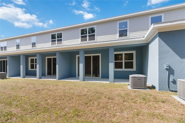 back of property with stucco siding, a lawn, and central air condition unit