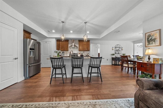 16386 Heron Hills Dr, Spring Hill, FL 34610 - kitchen with high end fridge, a raised ceiling, wall chimney range hood, dark wood-type flooring, and a breakfast bar area
