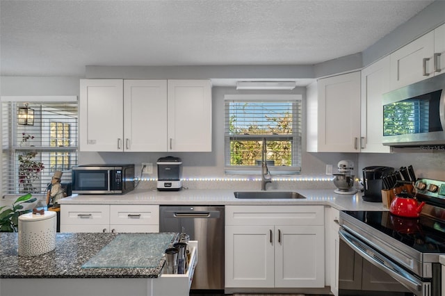 kitchen with a sink, stainless steel appliances, a textured ceiling, and white cabinetry