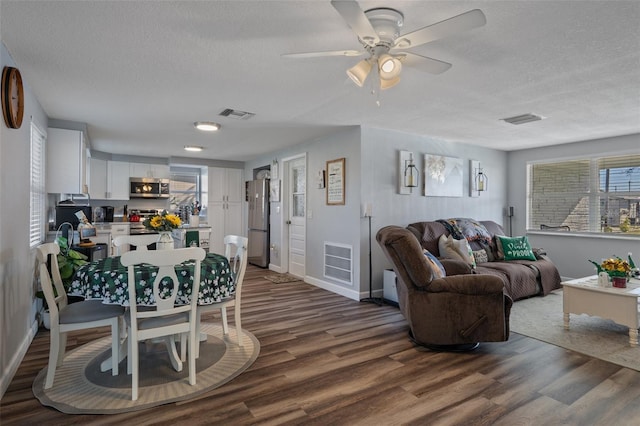 living room with dark wood finished floors, visible vents, a textured ceiling, and ceiling fan