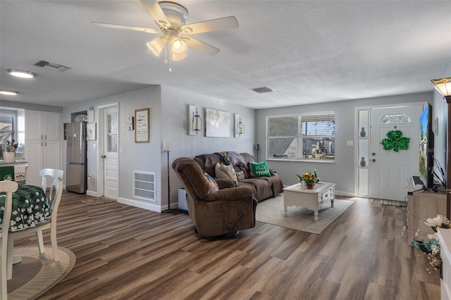 living room with dark wood finished floors, visible vents, a textured ceiling, and ceiling fan