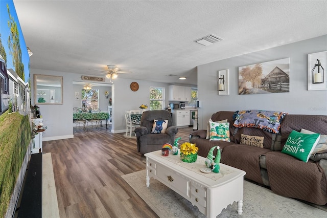 living area featuring visible vents, a textured ceiling, a ceiling fan, and wood finished floors