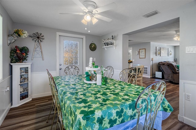 dining area featuring visible vents, dark wood finished floors, a wainscoted wall, a textured ceiling, and a ceiling fan