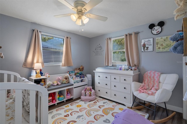 bedroom with a nursery area, wood finished floors, baseboards, and ceiling fan