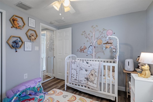 bedroom featuring a nursery area, wood finished floors, visible vents, and ceiling fan