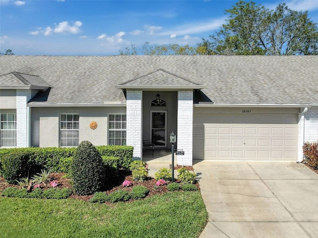 ranch-style house featuring concrete driveway, a garage, brick siding, and roof with shingles