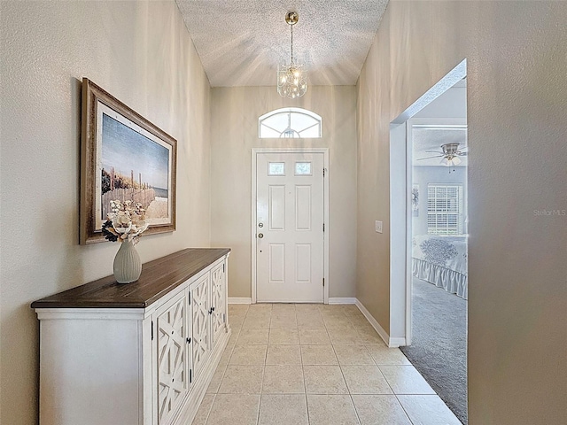 entrance foyer with light tile patterned flooring, a textured ceiling, baseboards, and a ceiling fan