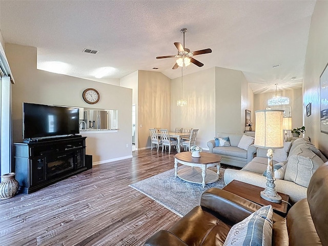 living room with visible vents, lofted ceiling, ceiling fan with notable chandelier, wood finished floors, and a textured ceiling