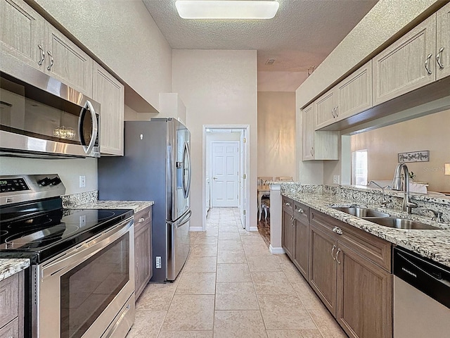 kitchen featuring light stone countertops, light tile patterned flooring, a sink, stainless steel appliances, and a textured ceiling