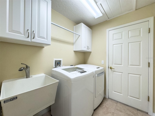 laundry area with light tile patterned floors, washing machine and clothes dryer, cabinet space, a sink, and a textured ceiling