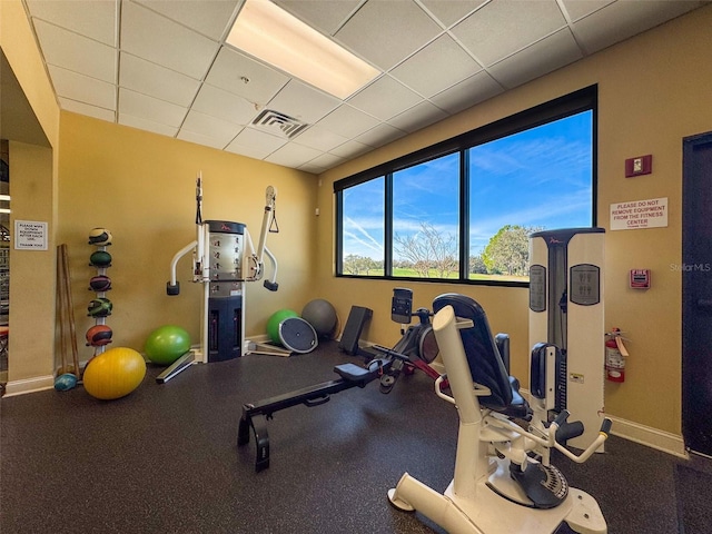 workout area with visible vents, a paneled ceiling, and baseboards