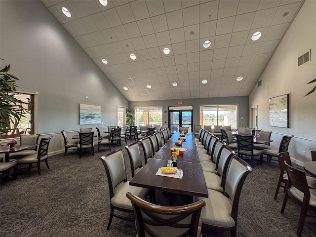 carpeted dining space with visible vents, a wealth of natural light, and high vaulted ceiling