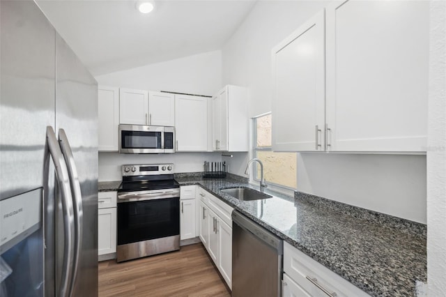 kitchen featuring dark stone countertops, lofted ceiling, a sink, stainless steel appliances, and white cabinetry