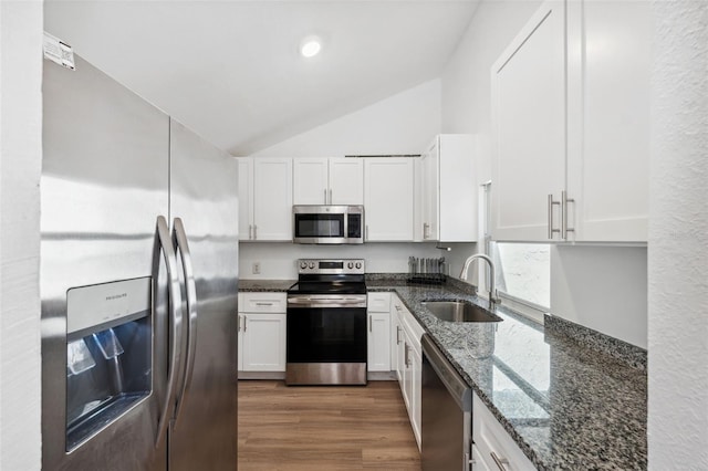 kitchen with white cabinetry, stainless steel appliances, dark stone counters, and a sink