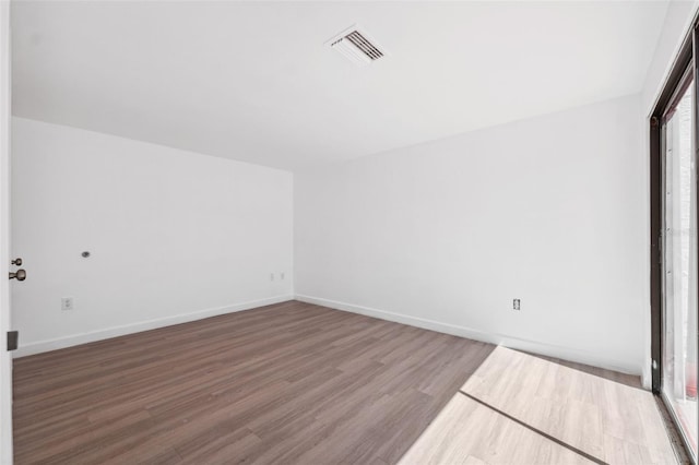 spare room with wood finished floors, visible vents, and baseboards