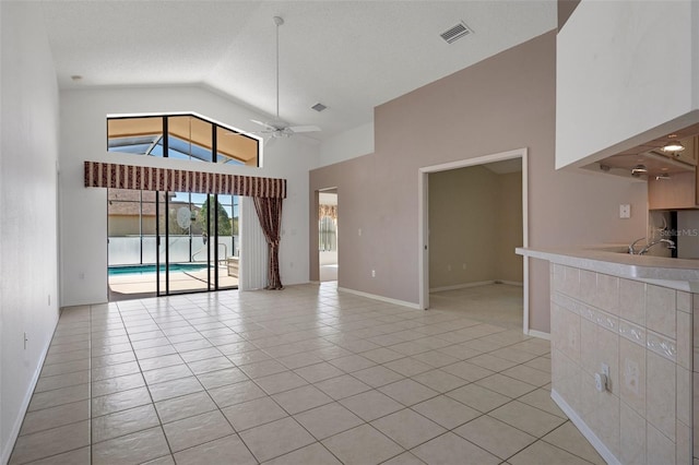 unfurnished living room featuring visible vents, high vaulted ceiling, a textured ceiling, light tile patterned floors, and ceiling fan