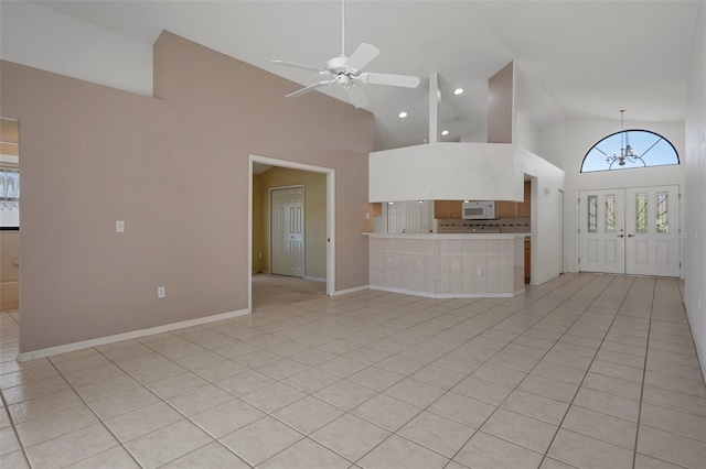 unfurnished living room featuring light tile patterned floors, ceiling fan with notable chandelier, baseboards, and high vaulted ceiling