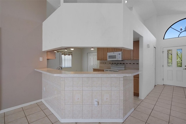 kitchen with backsplash, light countertops, light tile patterned floors, white appliances, and high vaulted ceiling