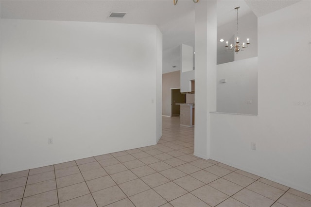 empty room with a notable chandelier, light tile patterned flooring, visible vents, and a towering ceiling