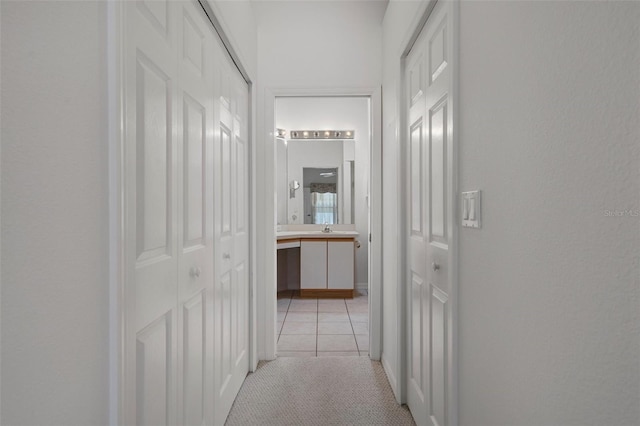 hallway featuring light tile patterned floors, light colored carpet, and a sink