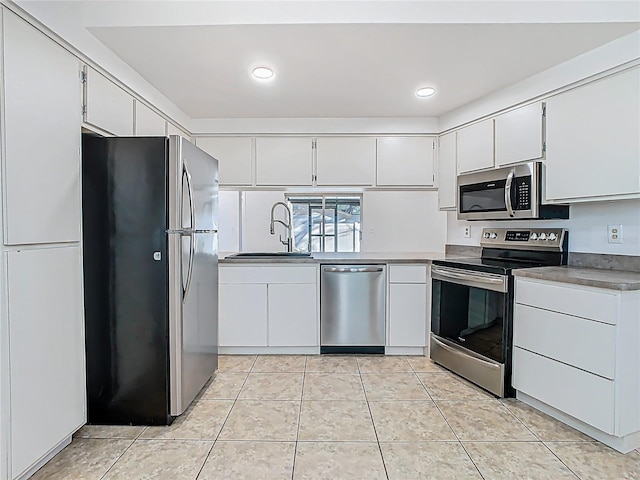 kitchen with a sink, white cabinets, light tile patterned flooring, and stainless steel appliances