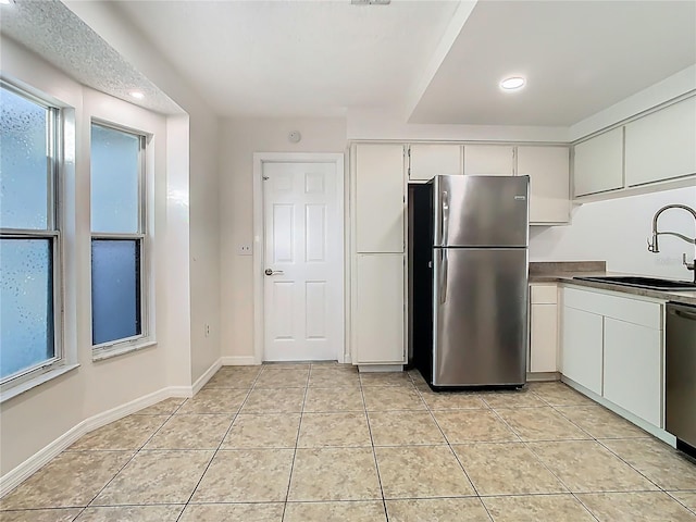 kitchen with a wealth of natural light, appliances with stainless steel finishes, light tile patterned flooring, white cabinetry, and a sink