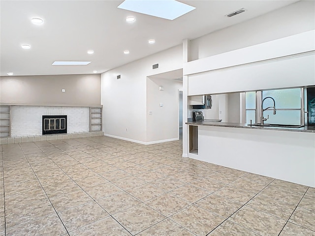 unfurnished living room with light tile patterned floors, visible vents, vaulted ceiling with skylight, recessed lighting, and a glass covered fireplace