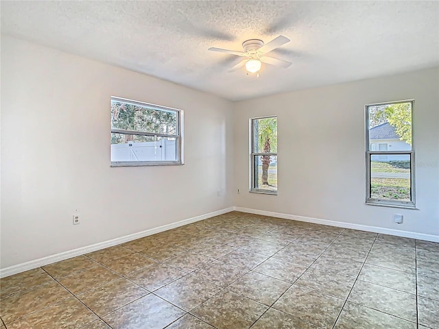 tiled empty room with baseboards, a textured ceiling, and a ceiling fan