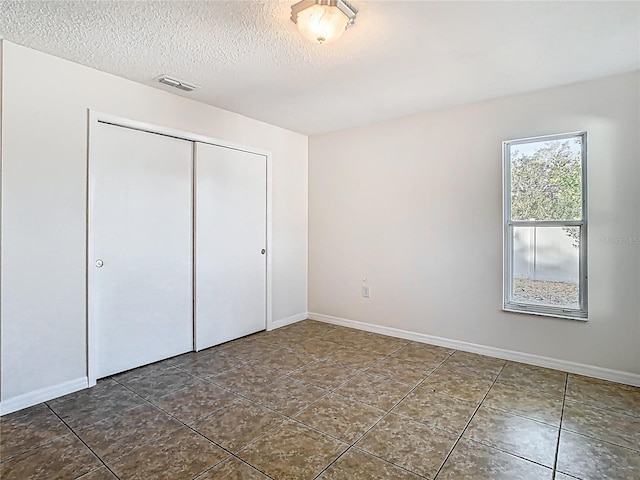 unfurnished bedroom with visible vents, baseboards, dark tile patterned floors, a closet, and a textured ceiling