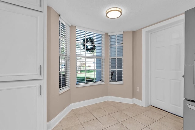 unfurnished dining area with light tile patterned floors, baseboards, and a textured ceiling