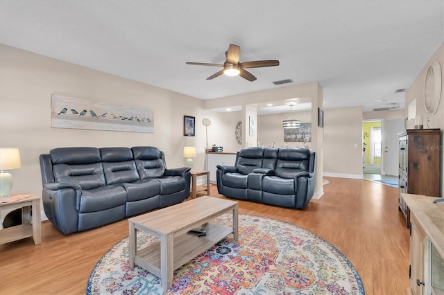 living room featuring visible vents, baseboards, ceiling fan, and light wood finished floors