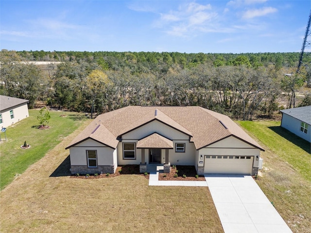 ranch-style home featuring a wooded view, concrete driveway, a front yard, a garage, and stone siding