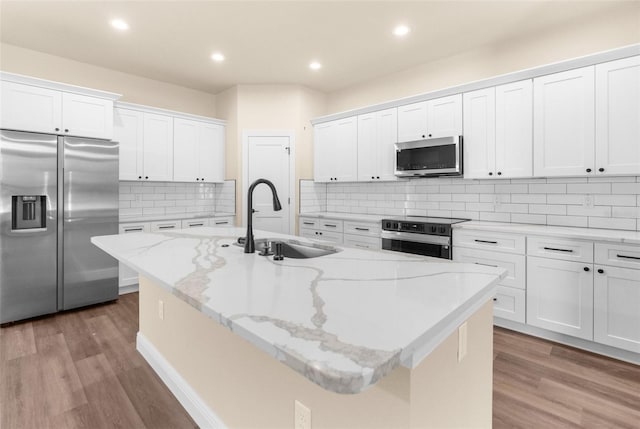 kitchen featuring an island with sink, a sink, wood finished floors, white cabinetry, and stainless steel appliances