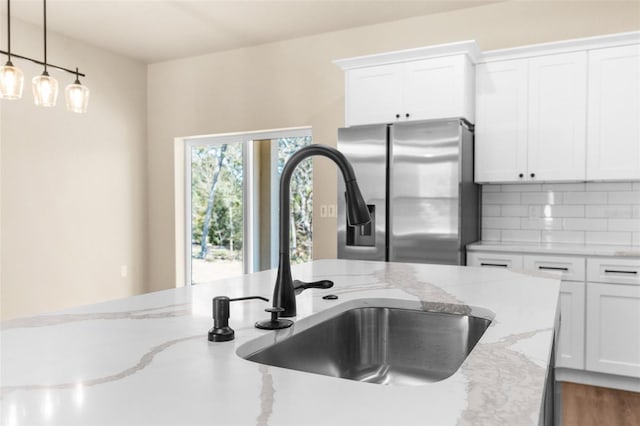 kitchen featuring a sink, decorative backsplash, stainless steel fridge, and white cabinetry