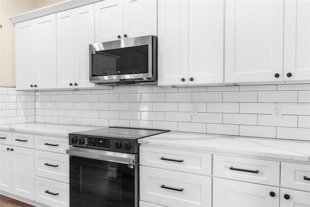 kitchen featuring stainless steel microwave, range with electric cooktop, white cabinetry, and decorative backsplash