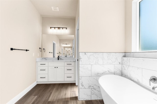 bathroom with visible vents, wood finished floors, tile walls, a soaking tub, and vanity