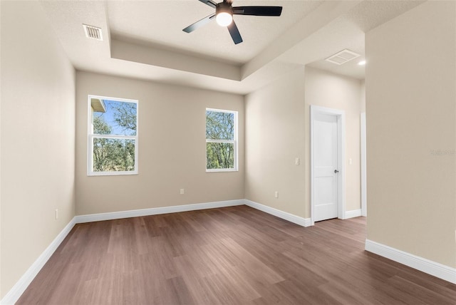 empty room featuring a ceiling fan, baseboards, visible vents, dark wood-style flooring, and a raised ceiling