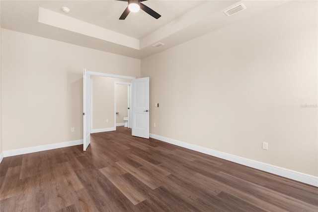 spare room with visible vents, a ceiling fan, a tray ceiling, baseboards, and dark wood-style flooring