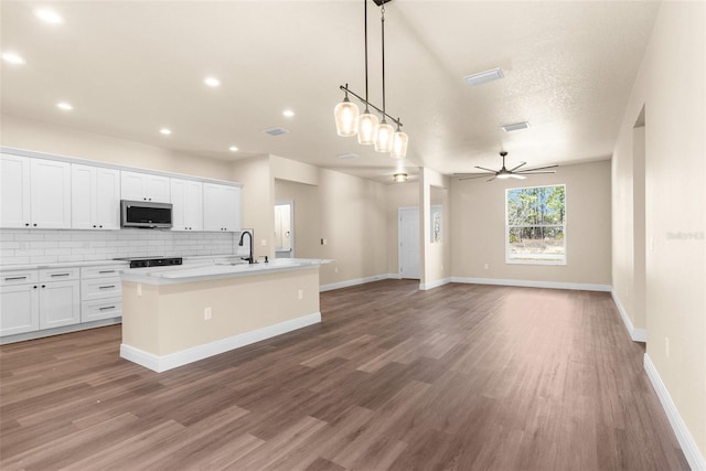 kitchen featuring an island with sink, white cabinetry, stainless steel microwave, open floor plan, and backsplash