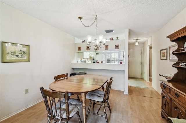 dining area featuring a chandelier, visible vents, a textured ceiling, and light wood-type flooring