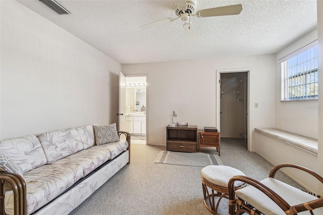 living area featuring visible vents, light colored carpet, a ceiling fan, and a textured ceiling