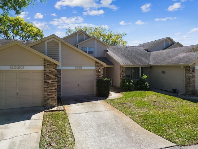 view of front of house with a front yard, a shingled roof, concrete driveway, a garage, and brick siding