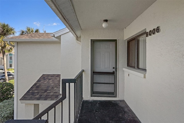 doorway to property with stucco siding and a shingled roof