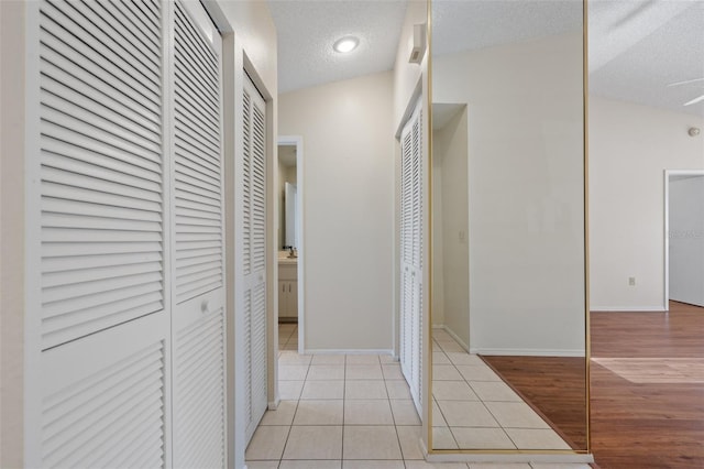 hall featuring light tile patterned floors, baseboards, and a textured ceiling