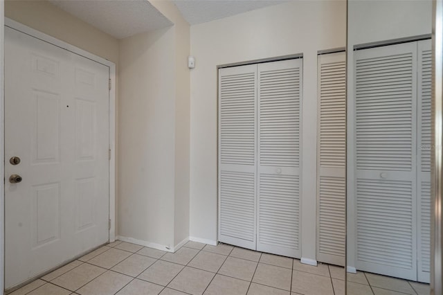 foyer entrance with light tile patterned flooring, a textured ceiling, and baseboards