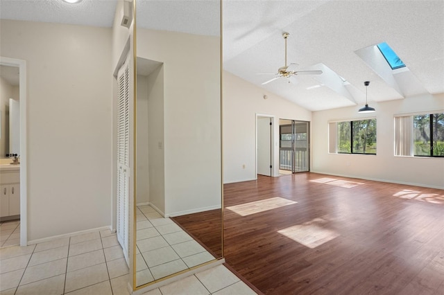 interior space featuring baseboards, vaulted ceiling with skylight, light tile patterned flooring, ceiling fan, and a textured ceiling