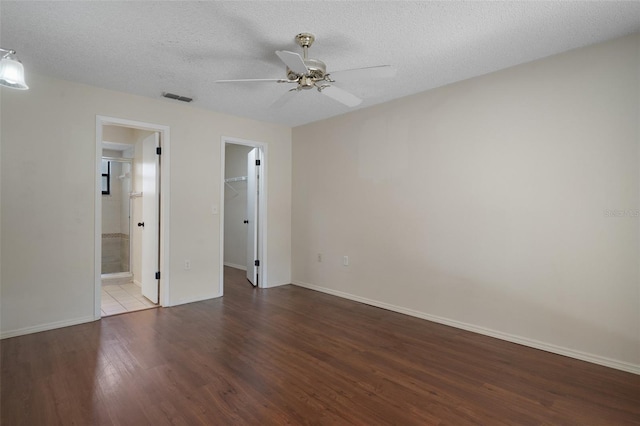 unfurnished bedroom with a spacious closet, visible vents, wood finished floors, a closet, and a textured ceiling