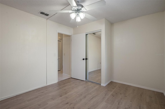 unfurnished bedroom with visible vents, light wood-style floors, a closet, a textured ceiling, and a ceiling fan