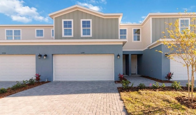 view of property featuring stucco siding, board and batten siding, decorative driveway, and a garage